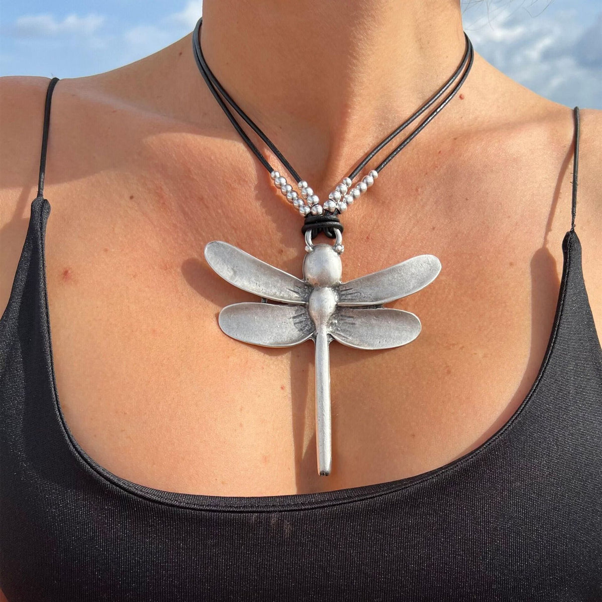 A close-up image of a silver beaded dragonfly pendant necklace with a black beaded chain.