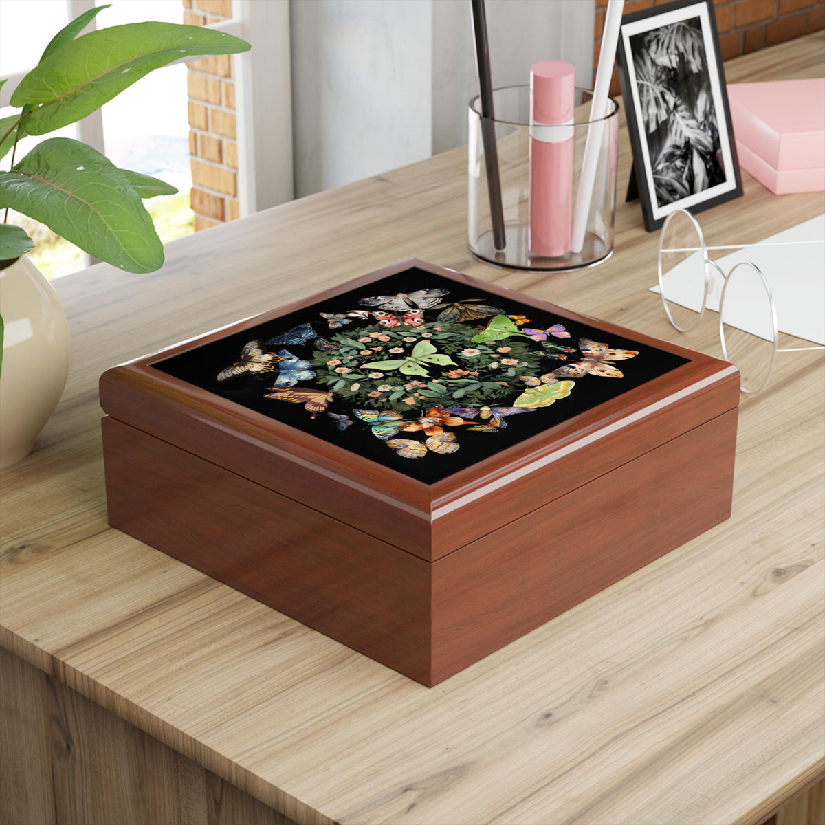 Angled view of a brown wooden luna moth jewelry box on a desk beside a plant and stationery.