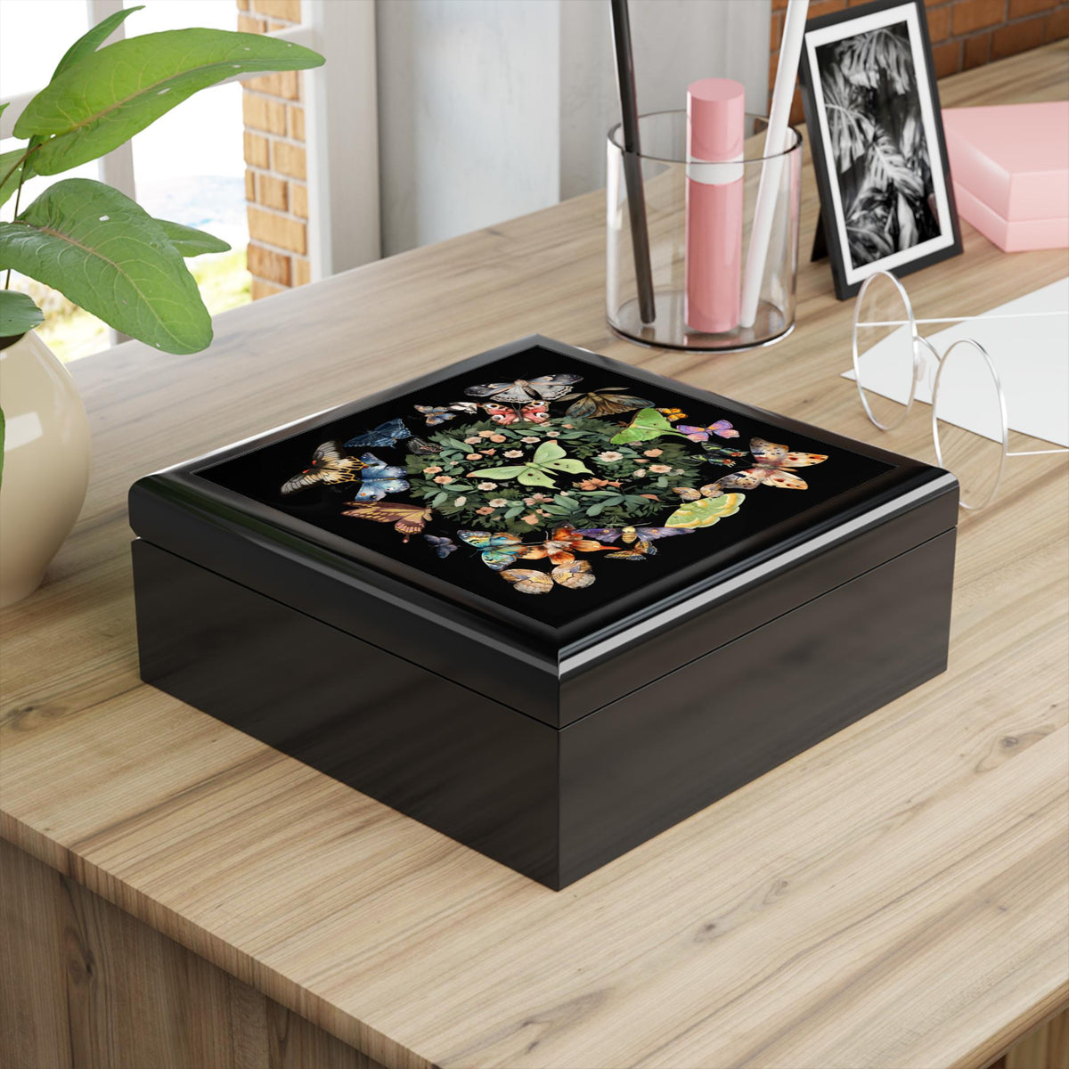 Angled view of a black luna moth jewelry box with colorful butterflies on the lid beside desk stationery.