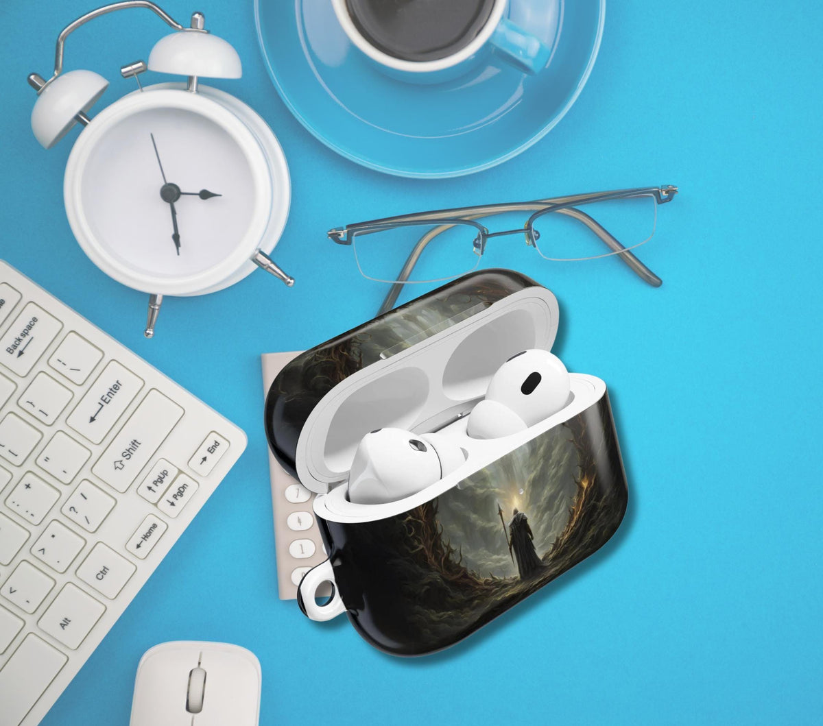 A custom protective AirPods case with a dark fantasy scene print, shown open with white AirPods inside. The case is styled in a flat-lay arrangement on a bright blue background alongside a keyboard, mouse, glasses, a clock, and a coffee cup.