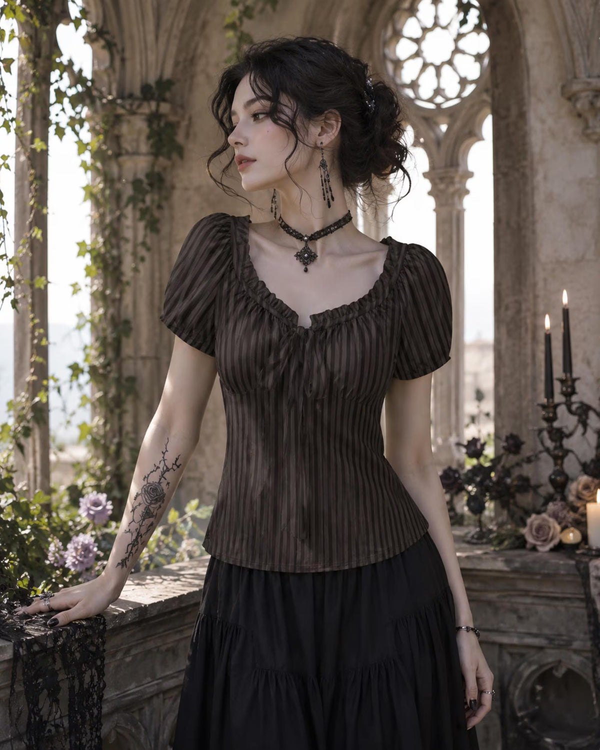 A woman stands in a gothic stone interior wearing a dark brown pleated short-sleeve top with a ruffled sweetheart neckline and a black skirt. She wears a black choker necklace and dangling earrings, with tattoos visible on her left arm.
