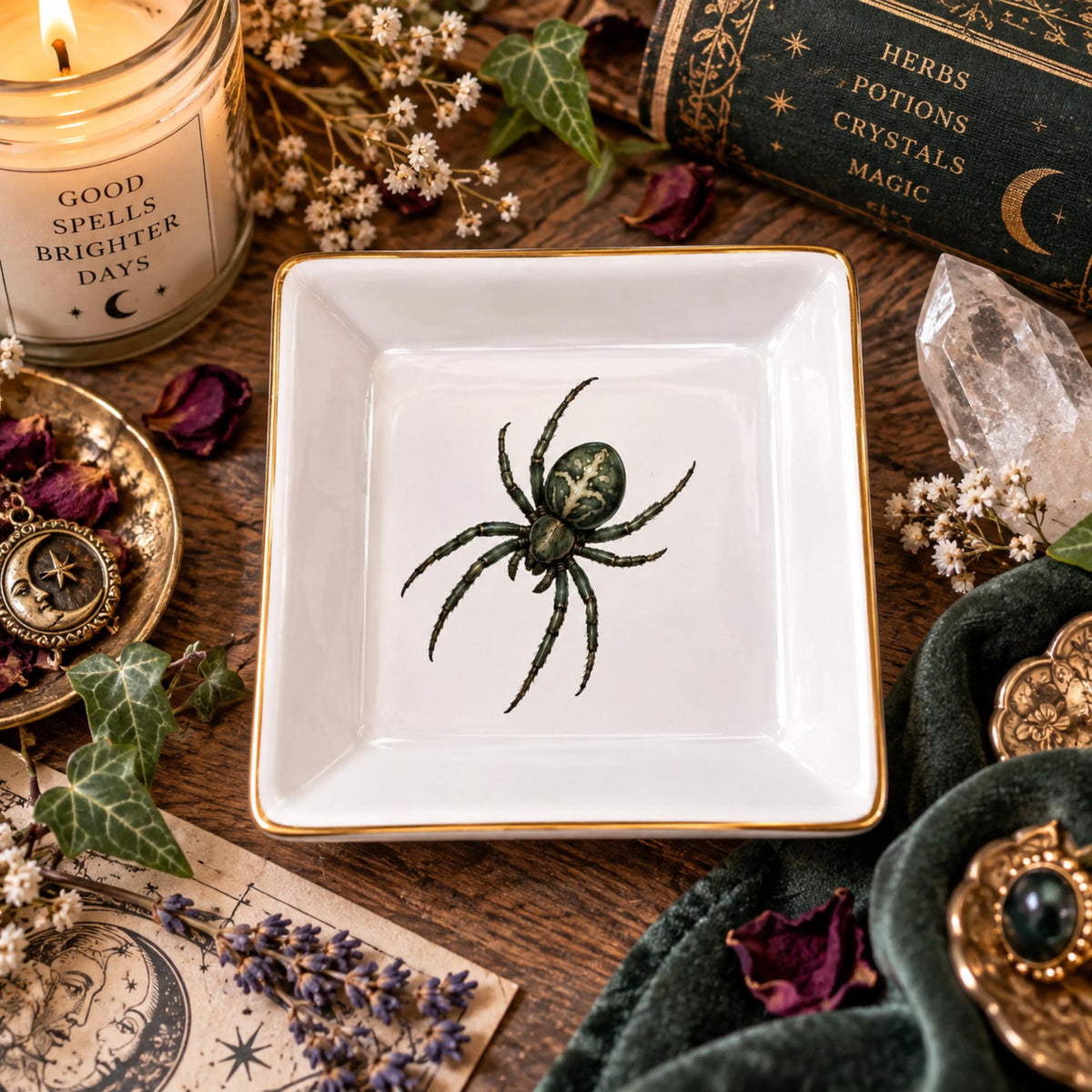Overhead view of an empty white gold-rimmed spider jewelry dish beside a candle and crystals on a wooden table.