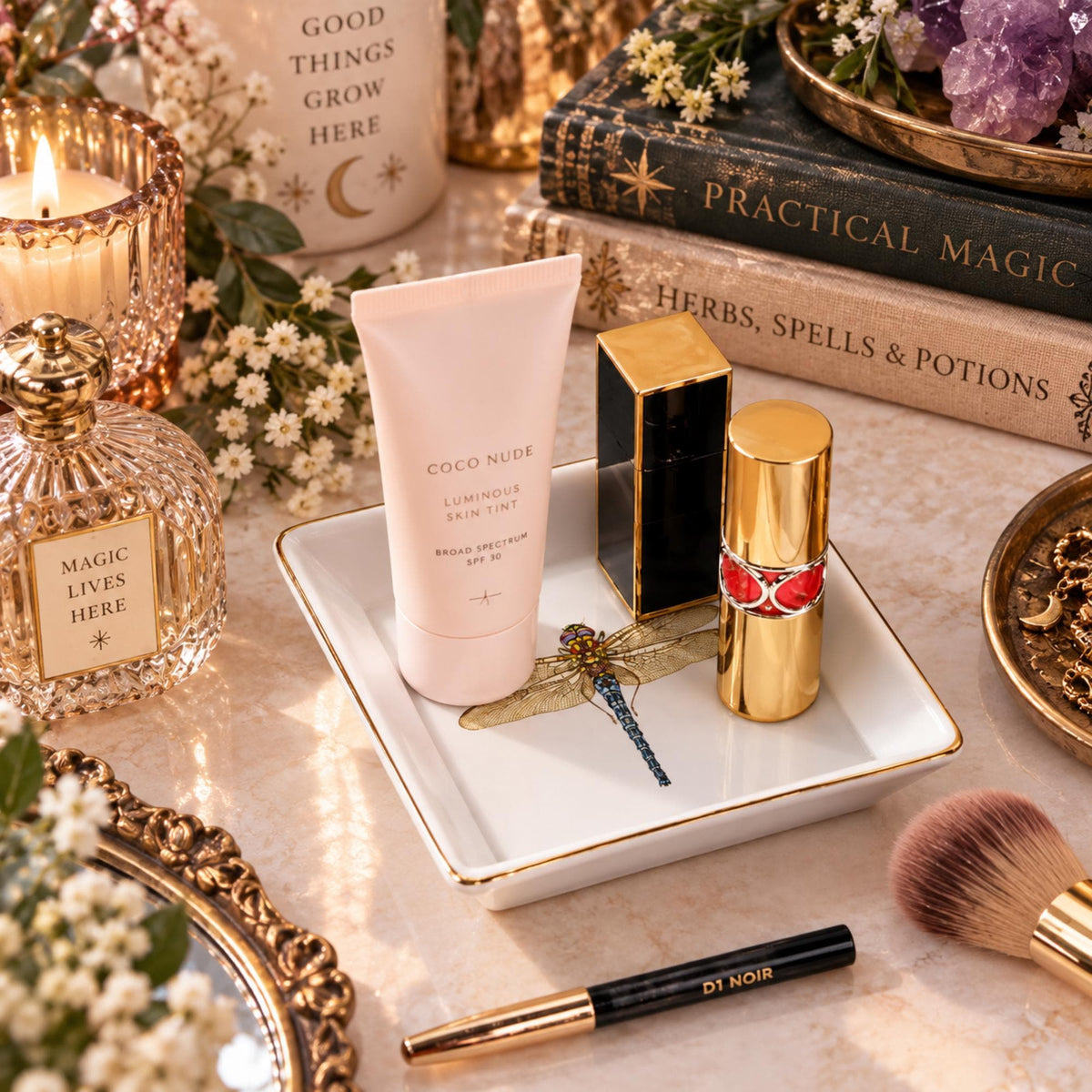 White square dragonfly jewelry dish holding cosmetics on a vanity beside a mirror and candle.