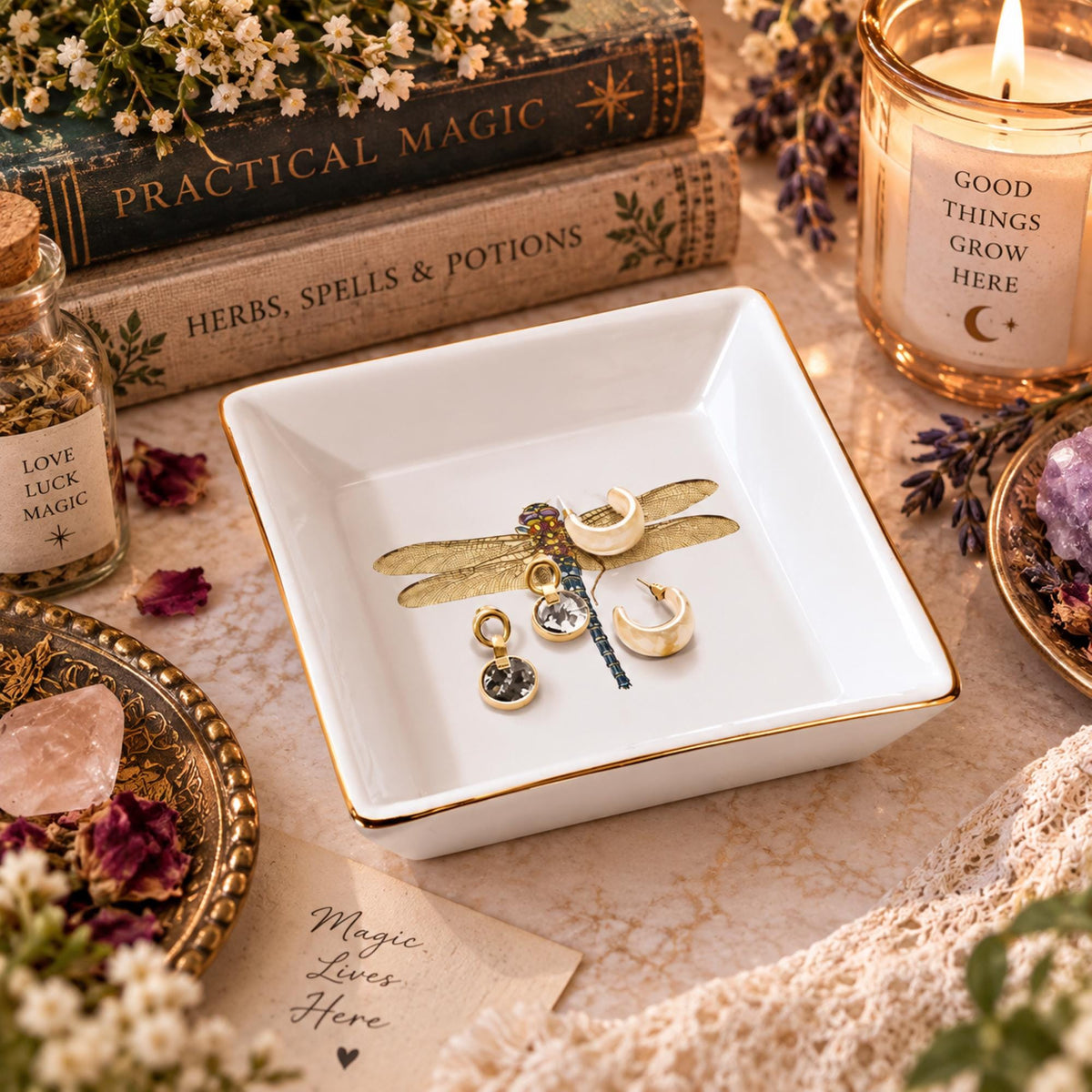 Empty white square dragonfly jewelry dish beside a pink lotion bottle and facial roller on a floral vanity.